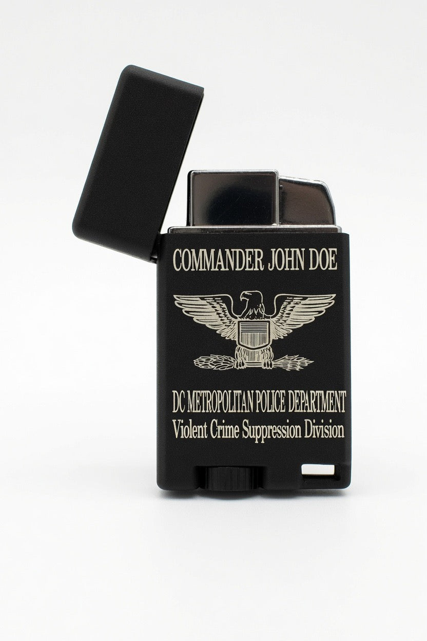 A black lighter with a hinged lid open, featuring gold-colored text and an eagle emblem. The text reads 'COMMANDER JOHN DOE' and 'DC METROPOLITAN POLICE DEPARTMENT Violent Crime Suppression Division'.
