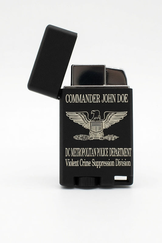 A black lighter with a hinged lid open, featuring gold-colored text and an eagle emblem. The text reads 'COMMANDER JOHN DOE' and 'DC METROPOLITAN POLICE DEPARTMENT Violent Crime Suppression Division'.